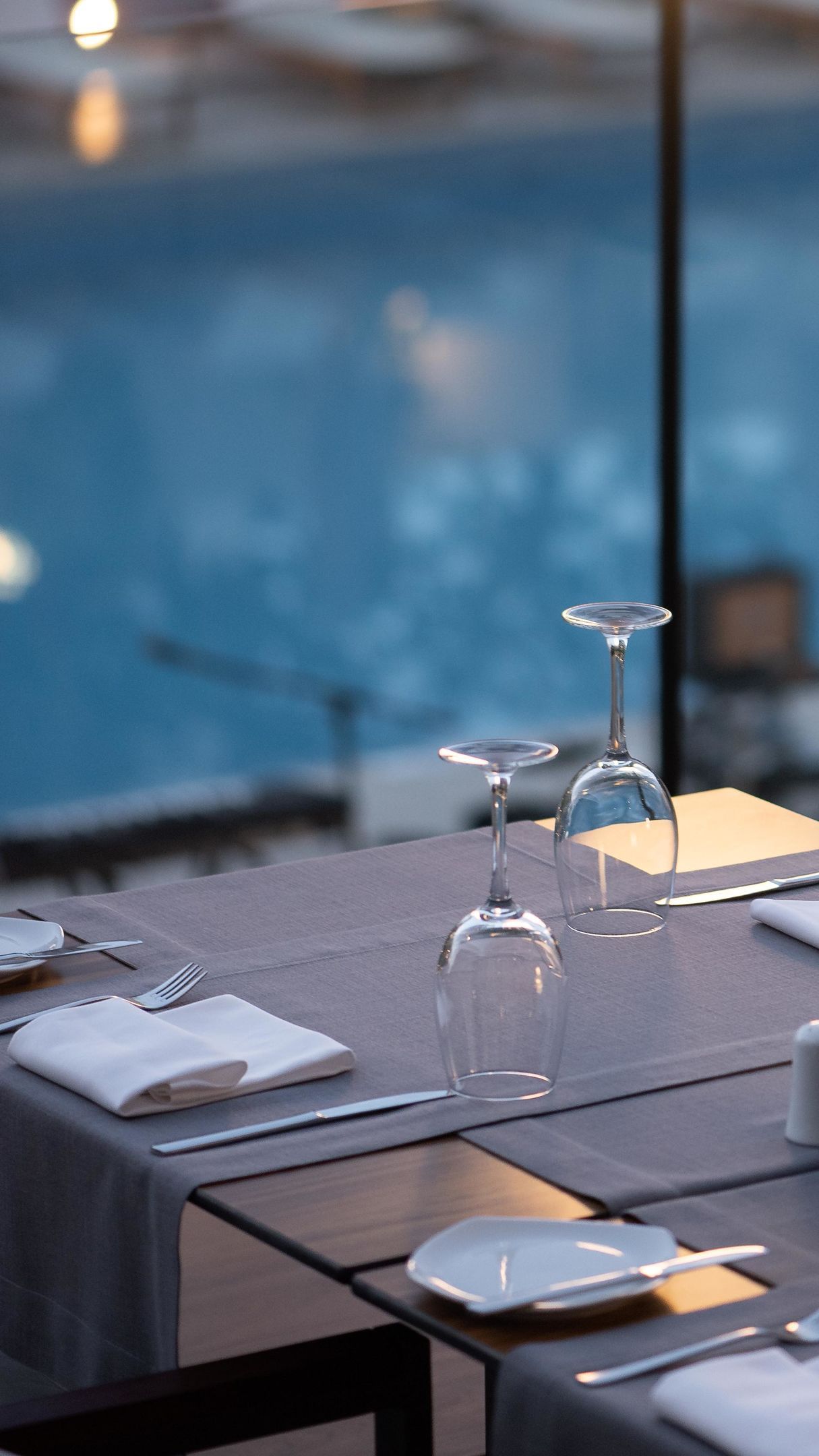 Ein Esszimmer mit Tisch, Weingläsern, Tellern und Besteck, mit Blick auf einen Poolbereich.