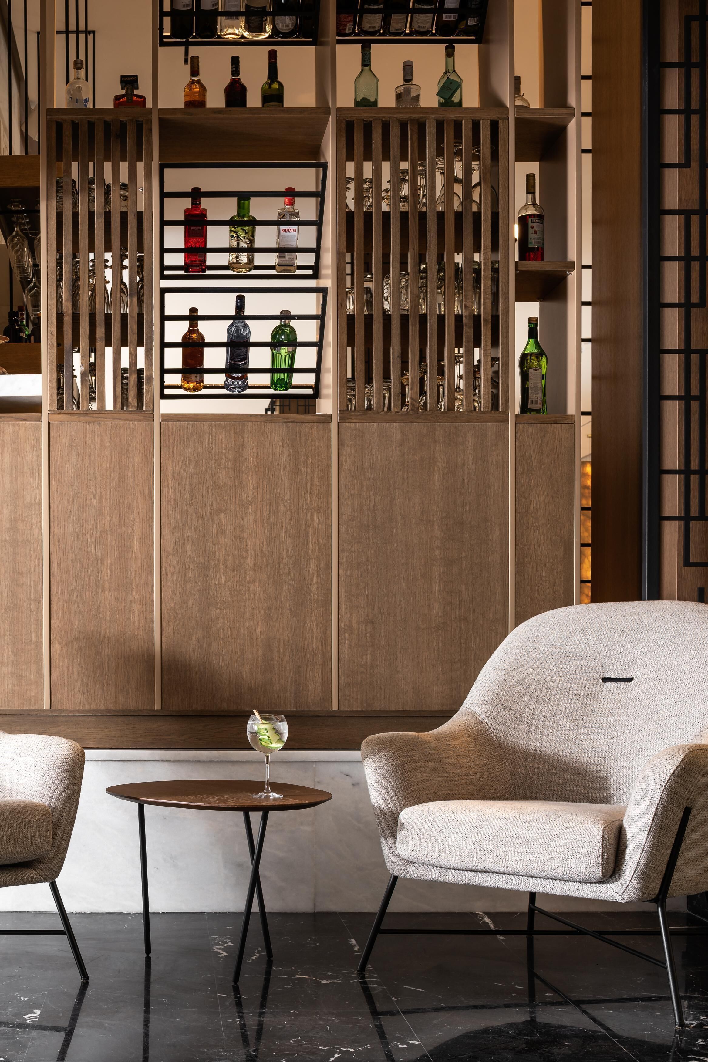 Un interior moderno con un separador de madera que exhibe varias botellas, una mesa redonda con una silla y una copa de vino.