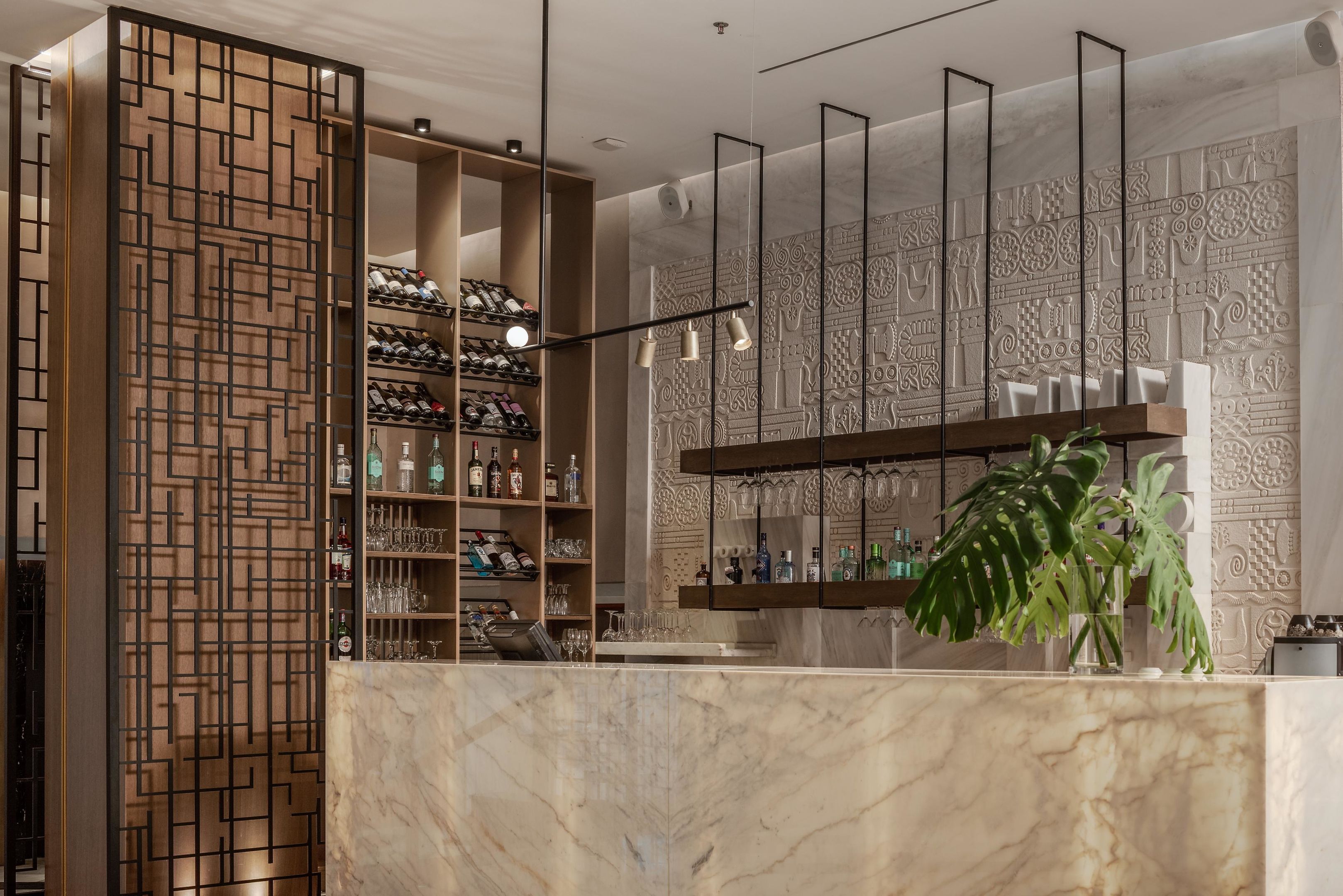 A bar area with shelves of bottles and glasses, a marble counter, and a decorative wall with intricate patterns.