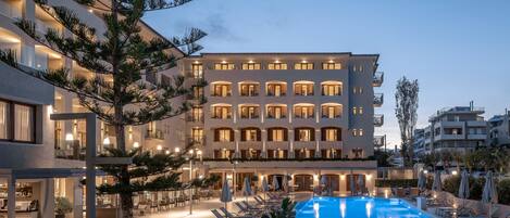 A hotel with a swimming pool, outdoor seating, and a well-lit facade.
