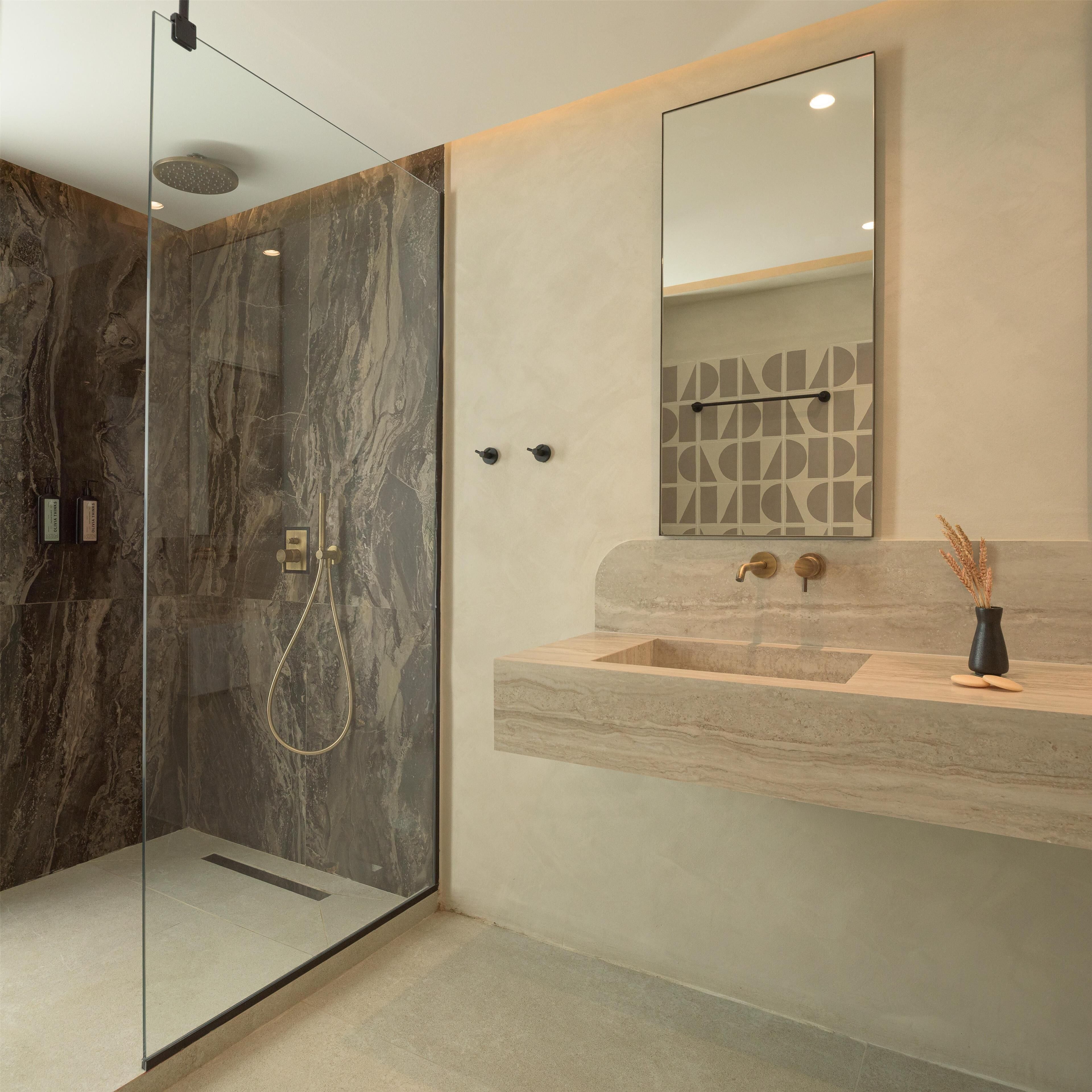 Ein modernes Badezimmer mit einer gläsernen Duschkabine, einer marmorierten Wand, einem Holzwaschtisch mit Waschbecken und einem Spiegel mit geometrischer Wandkunst.