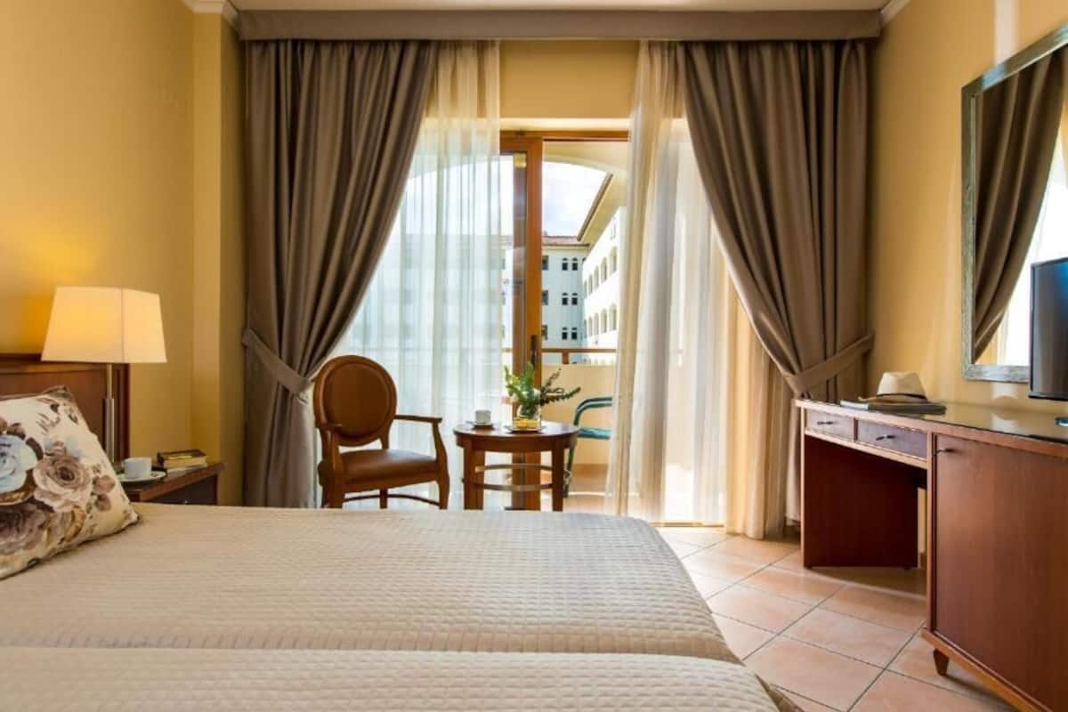 Une chambre d’hôtel comprenant un lit, un bureau, une chaise, une petite table avec une plante et un téléviseur.
