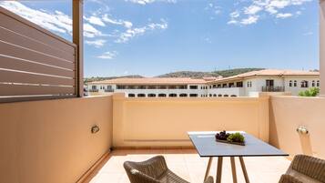 Un balcón con una mesa y dos sillas de mimbre, con vistas a un edificio de teja.