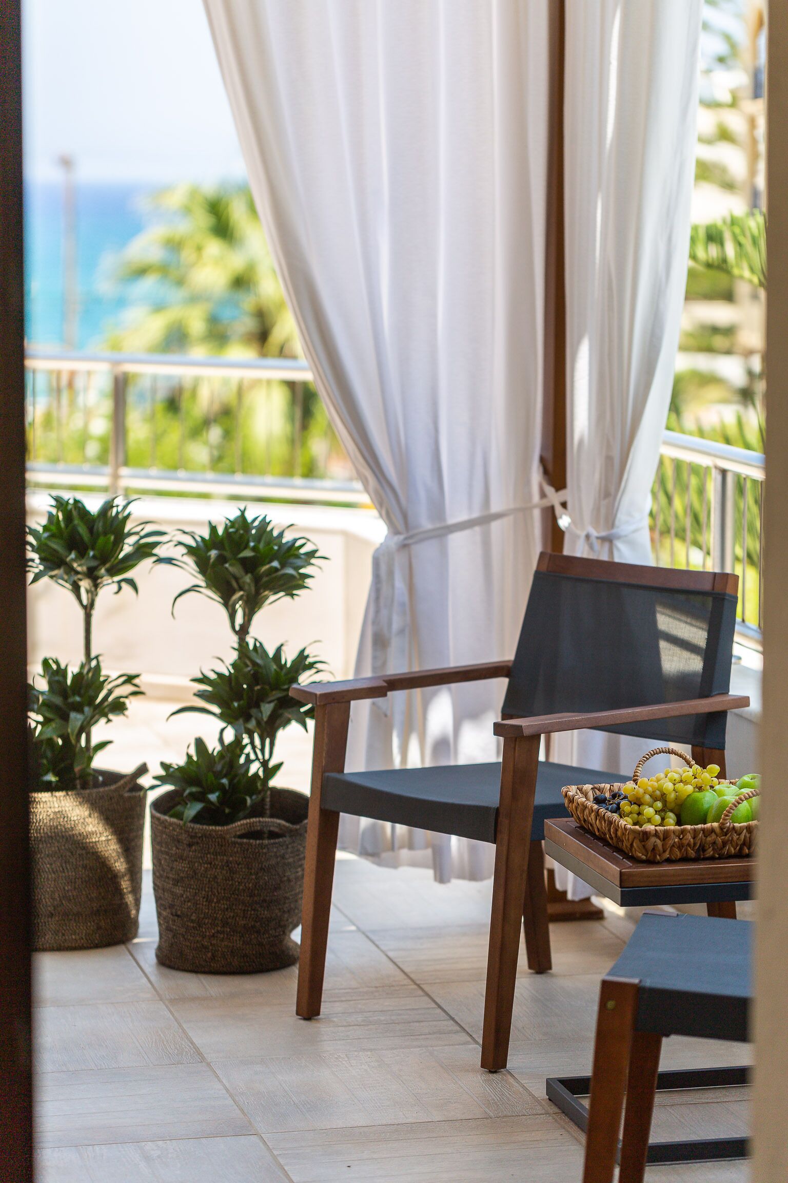 A balcony with a chair, potted plants, and a fruit basket.