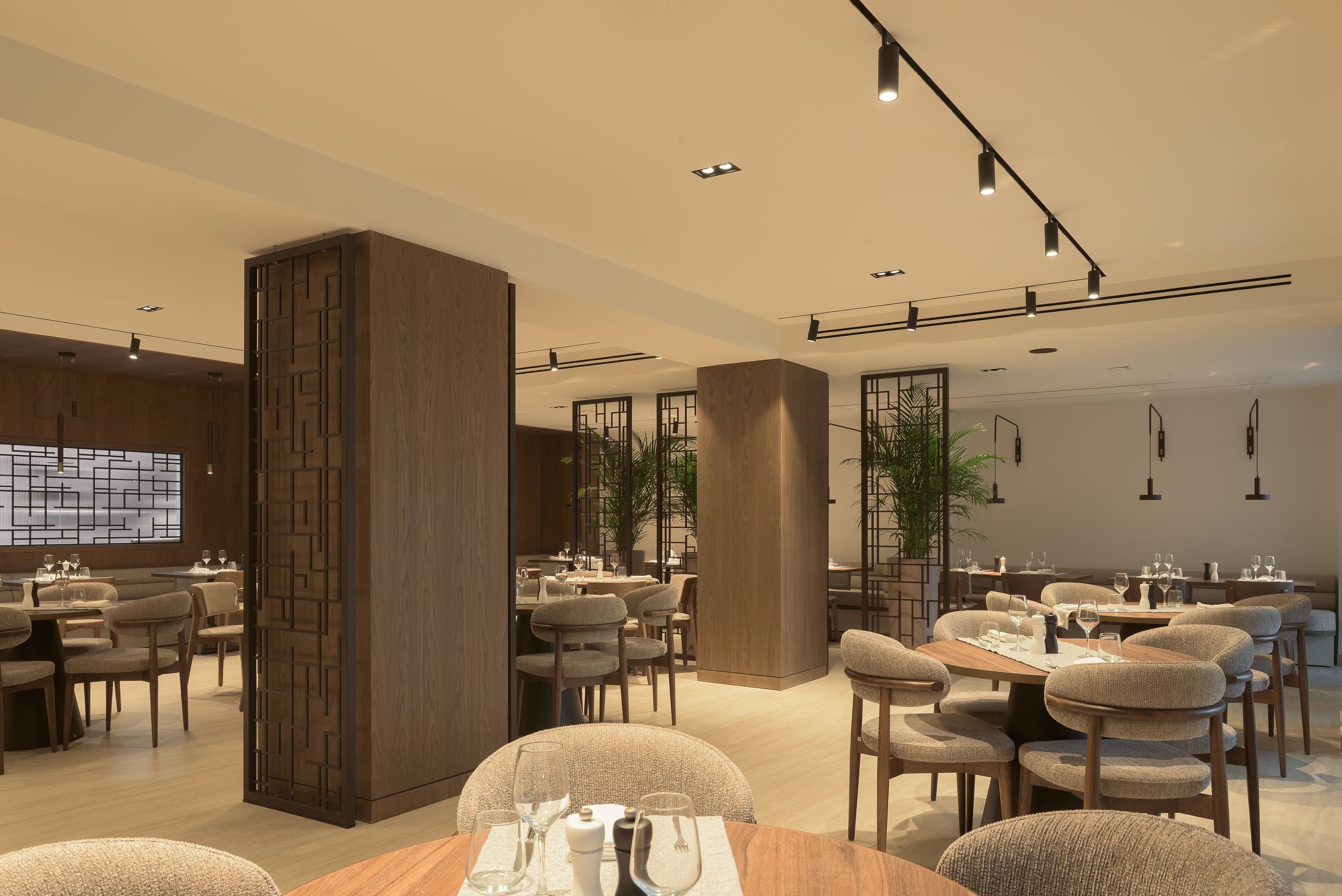 Un interior de restaurante moderno con mobiliario de madera, iluminación empotrada y una columna central.