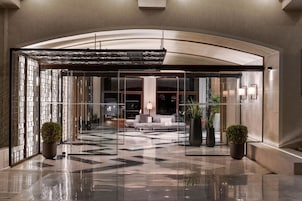 A modern lobby with a glass entrance, a seating area with a sofa, and potted plants.
