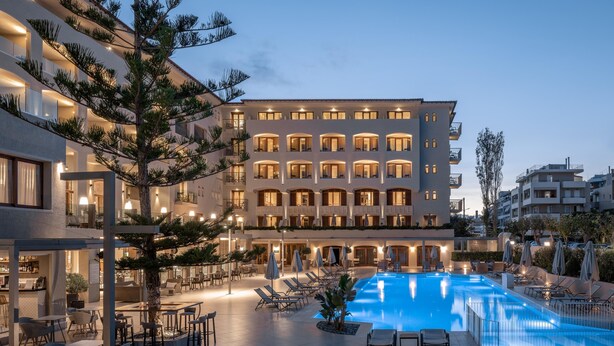 A hotel with a swimming pool, outdoor seating, and a well-lit facade.