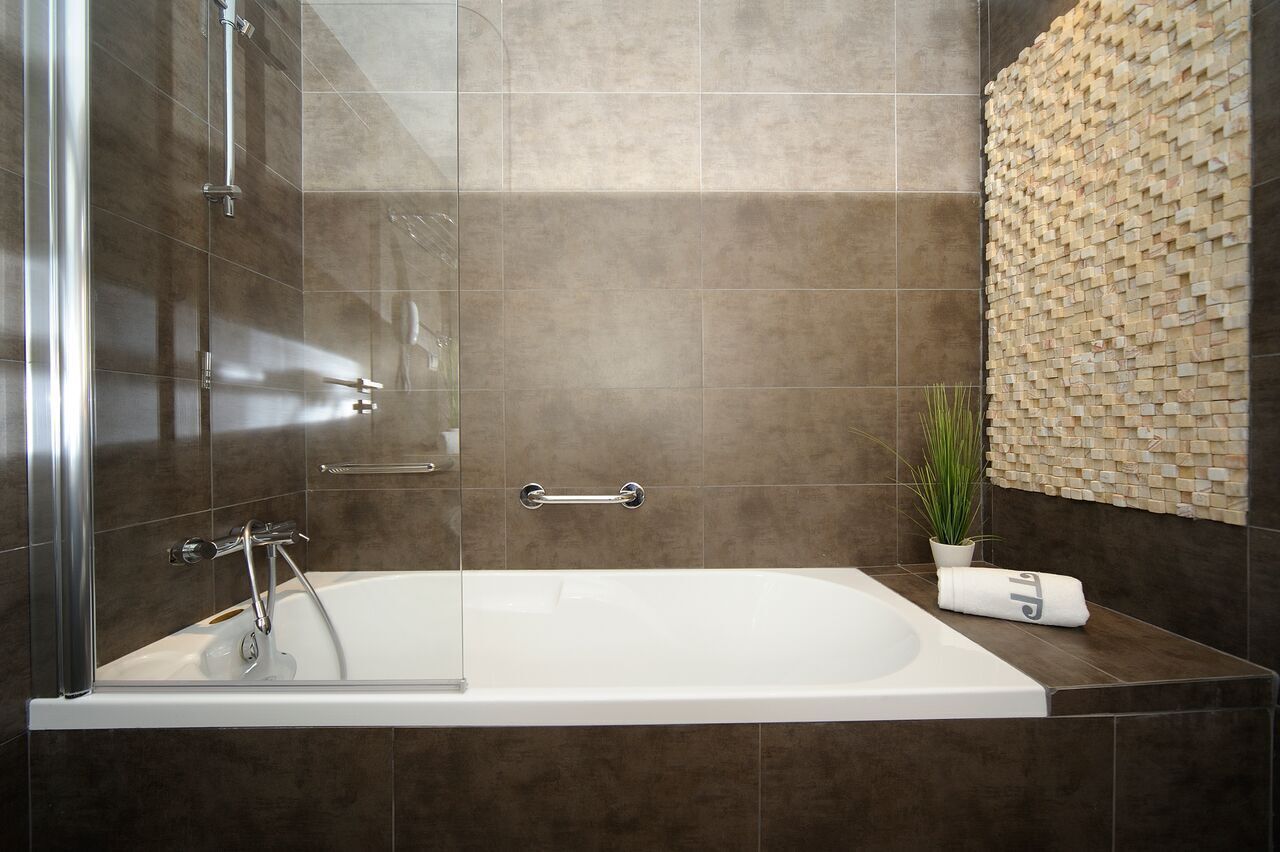 A modern bathroom with a glass-enclosed bathtub, a wall-mounted sink, and a decorative mosaic wall.