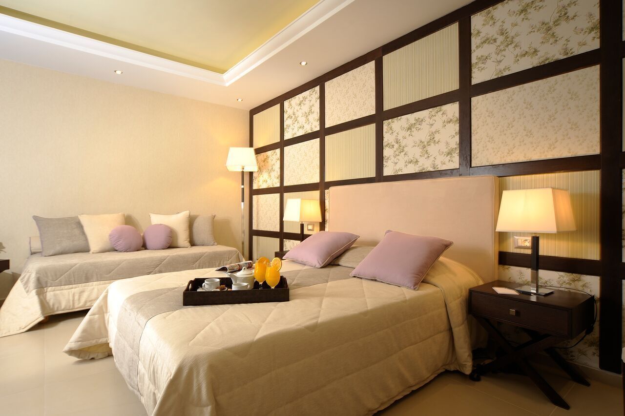 A hotel room with two beds, a nightstand, and a wall with a floral pattern.