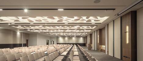 A conference room with rows of chairs, a patterned ceiling, and a neutral color scheme.