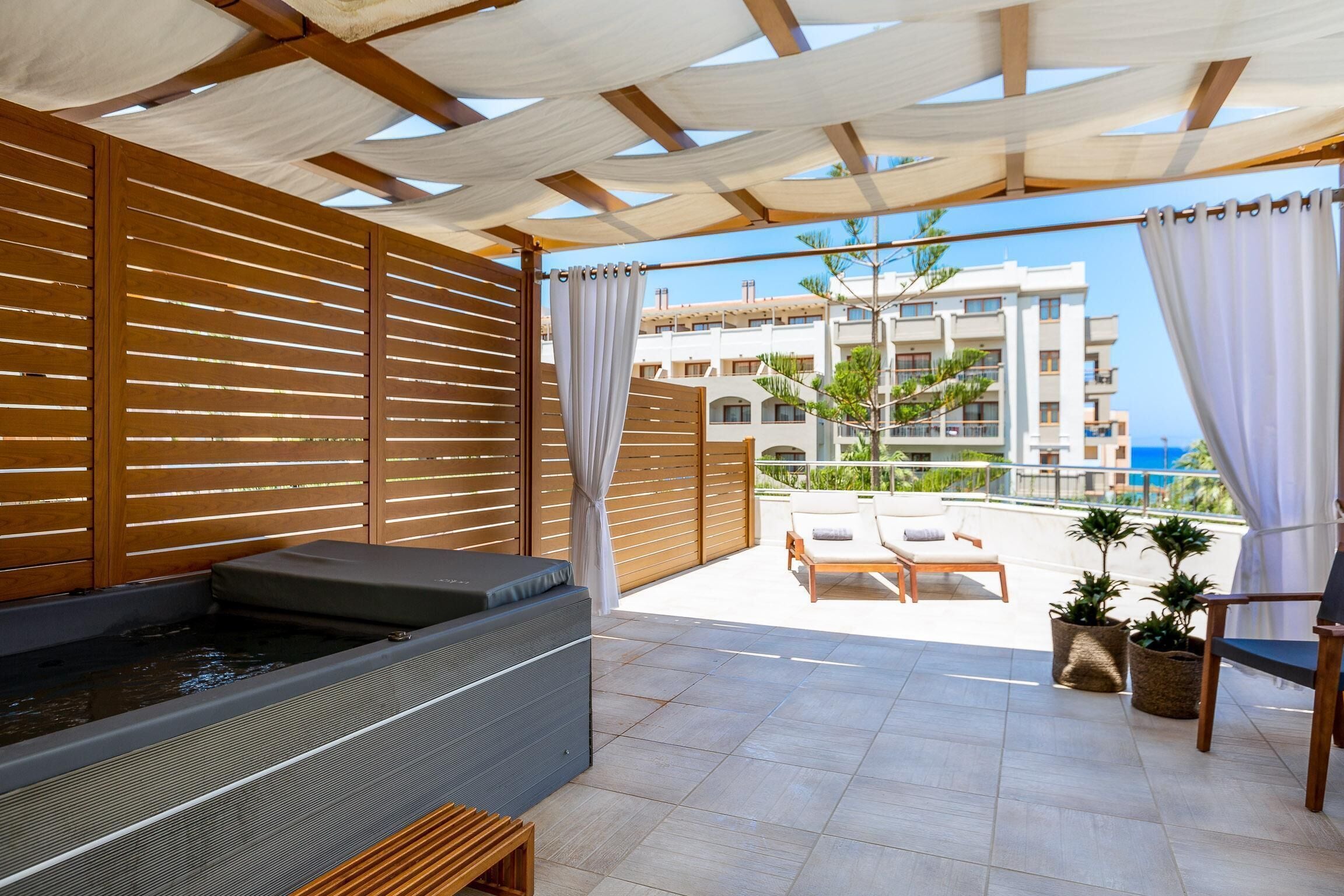 A spa area with a hot tub, wooden slatted walls, and a view of a building across a patio.