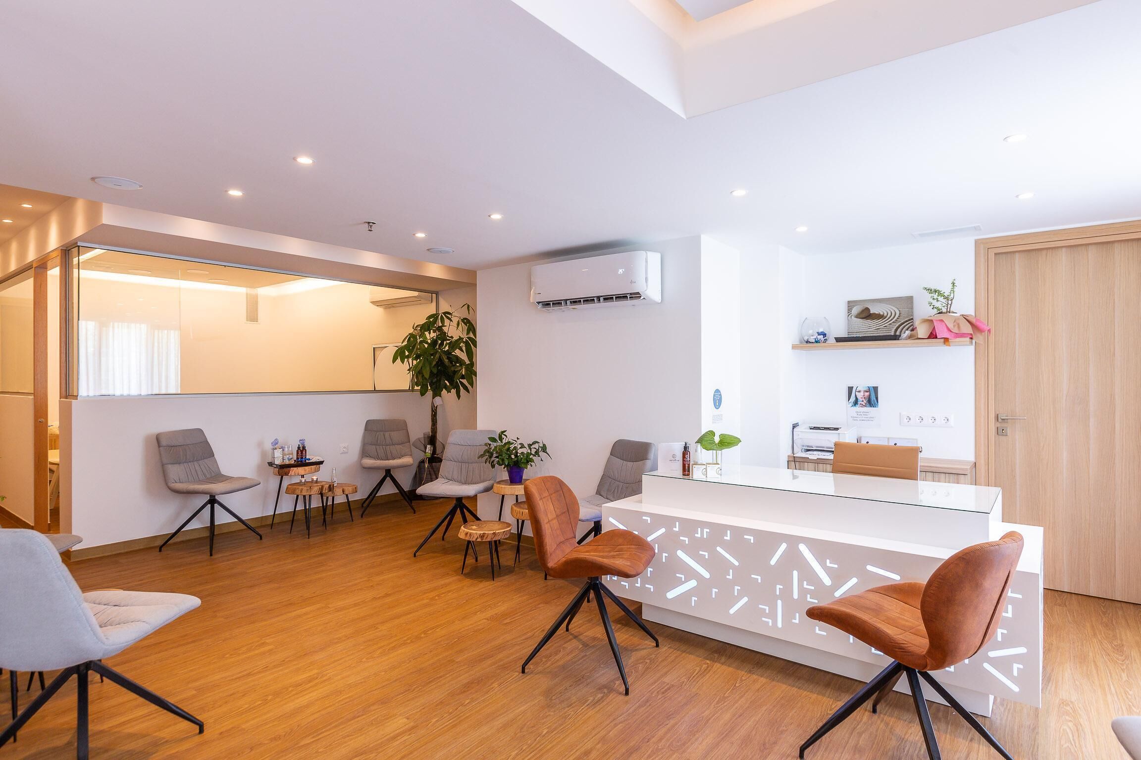 Un espace d’accueil moderne avec un comptoir en verre, un plancher en bois et des chaises au design contemporain.
