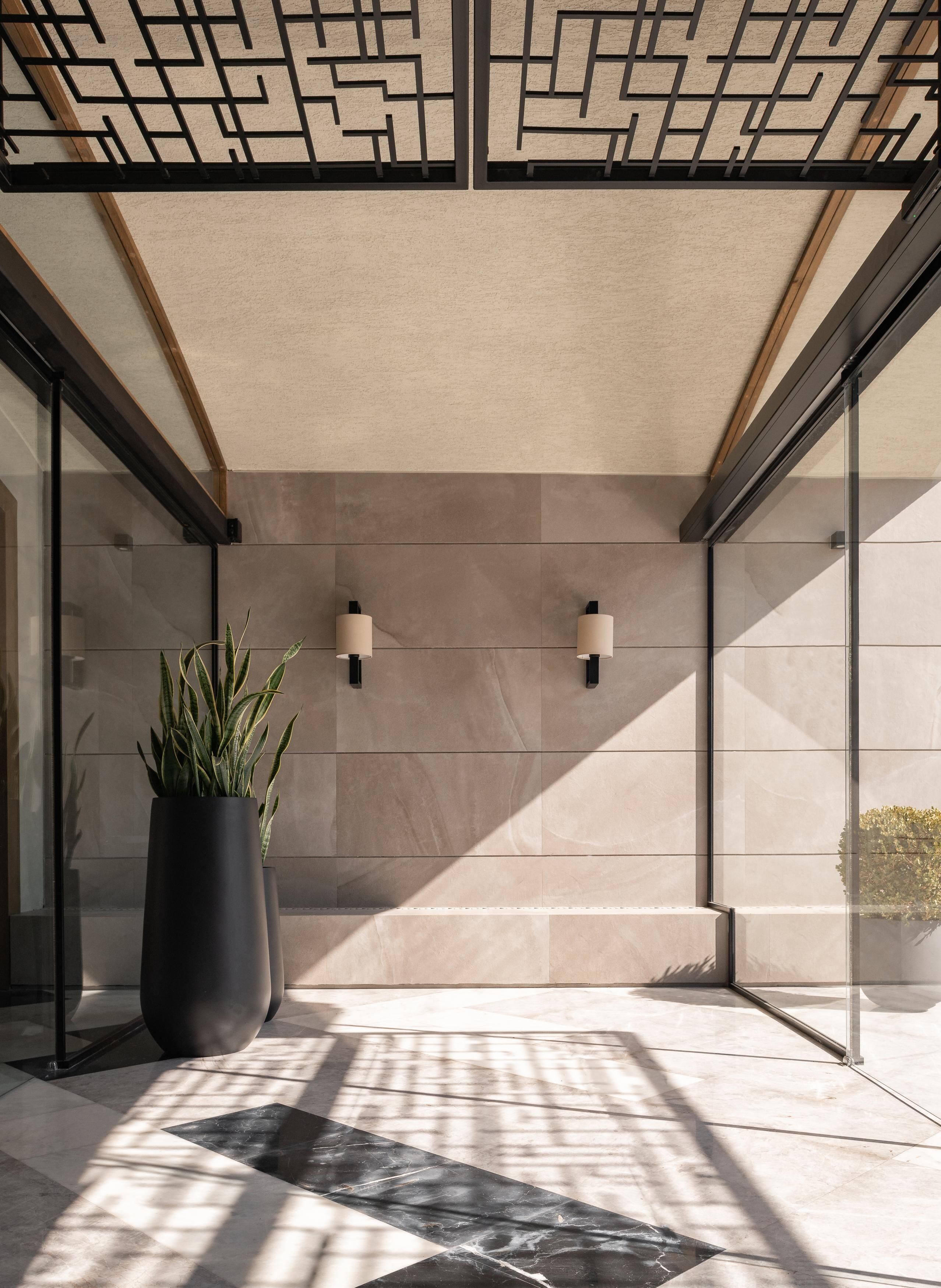A modern interior with a geometric ceiling design, a large potted plant, and a tiled floor.