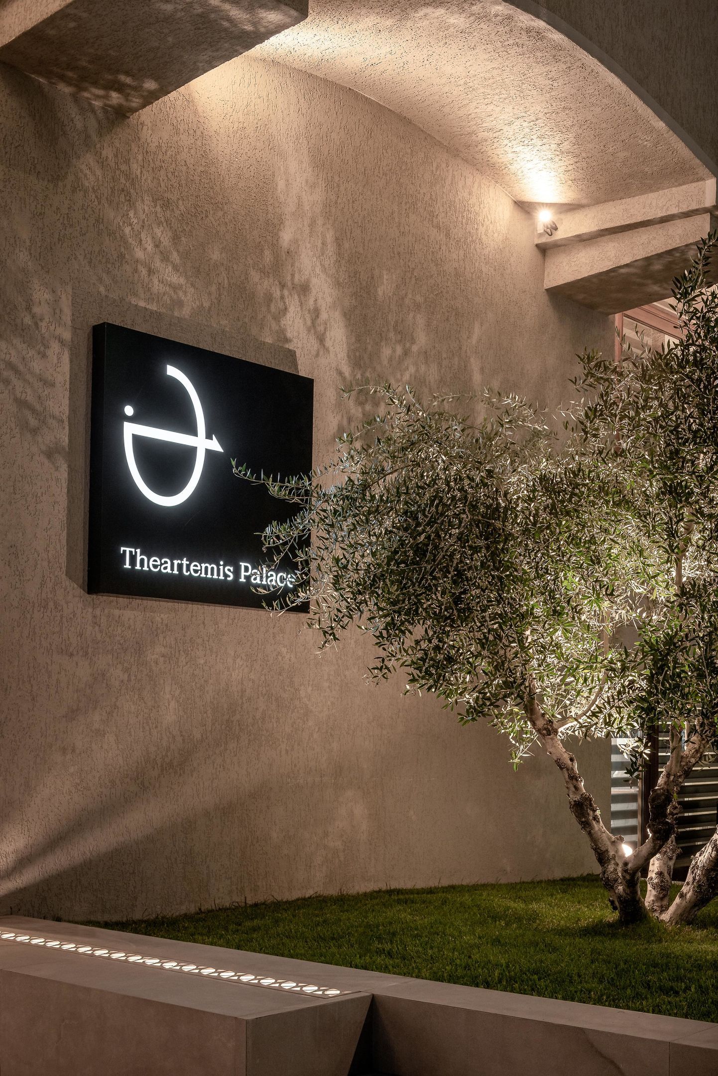 Schild für Theartemis Palace mit minimalistischem Design, einer Betonwand und einem kleinen Baum.