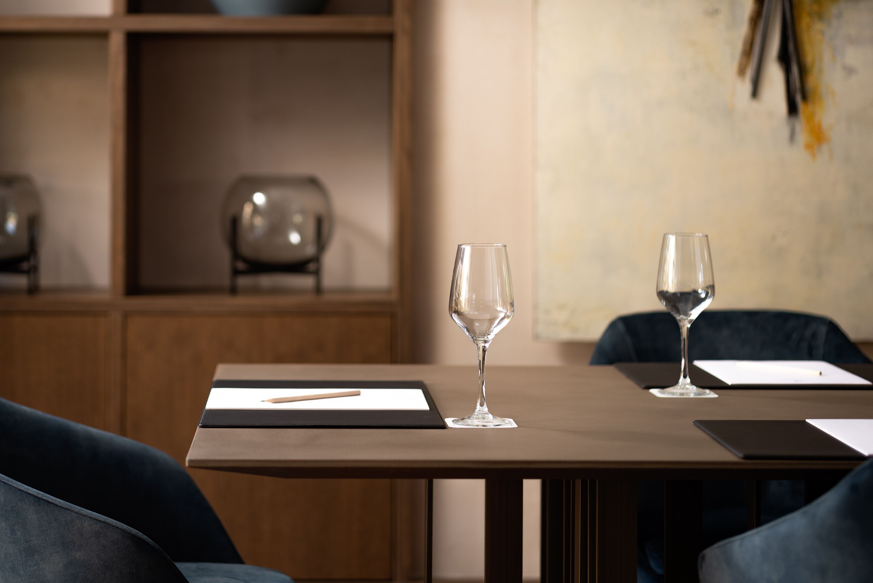 A modern dining area with a wooden table, two wine glasses, and a tablet on a black mat.