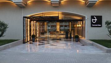 Entrada de hotel con fachada de vidrio, un letrero que indica Theartemis Palace y piso de baldosas.