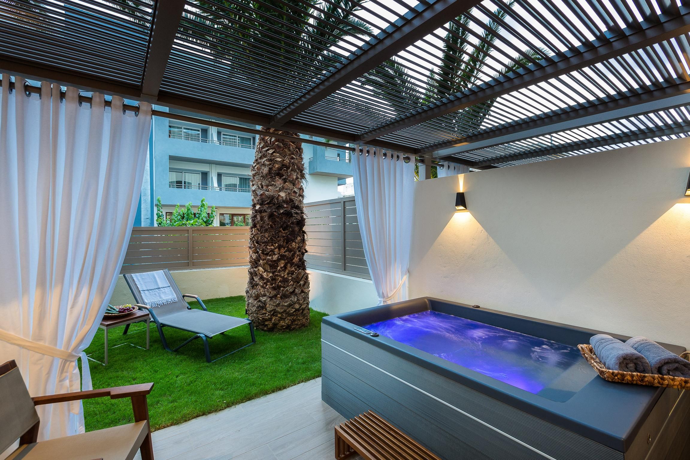 Un área de relajación exterior moderna con un jacuzzi, una silla de lounge y una mesita con frutas.