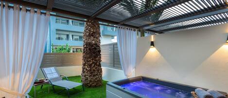 Un área de relajación exterior moderna con un jacuzzi, una silla de lounge y una mesita con frutas.