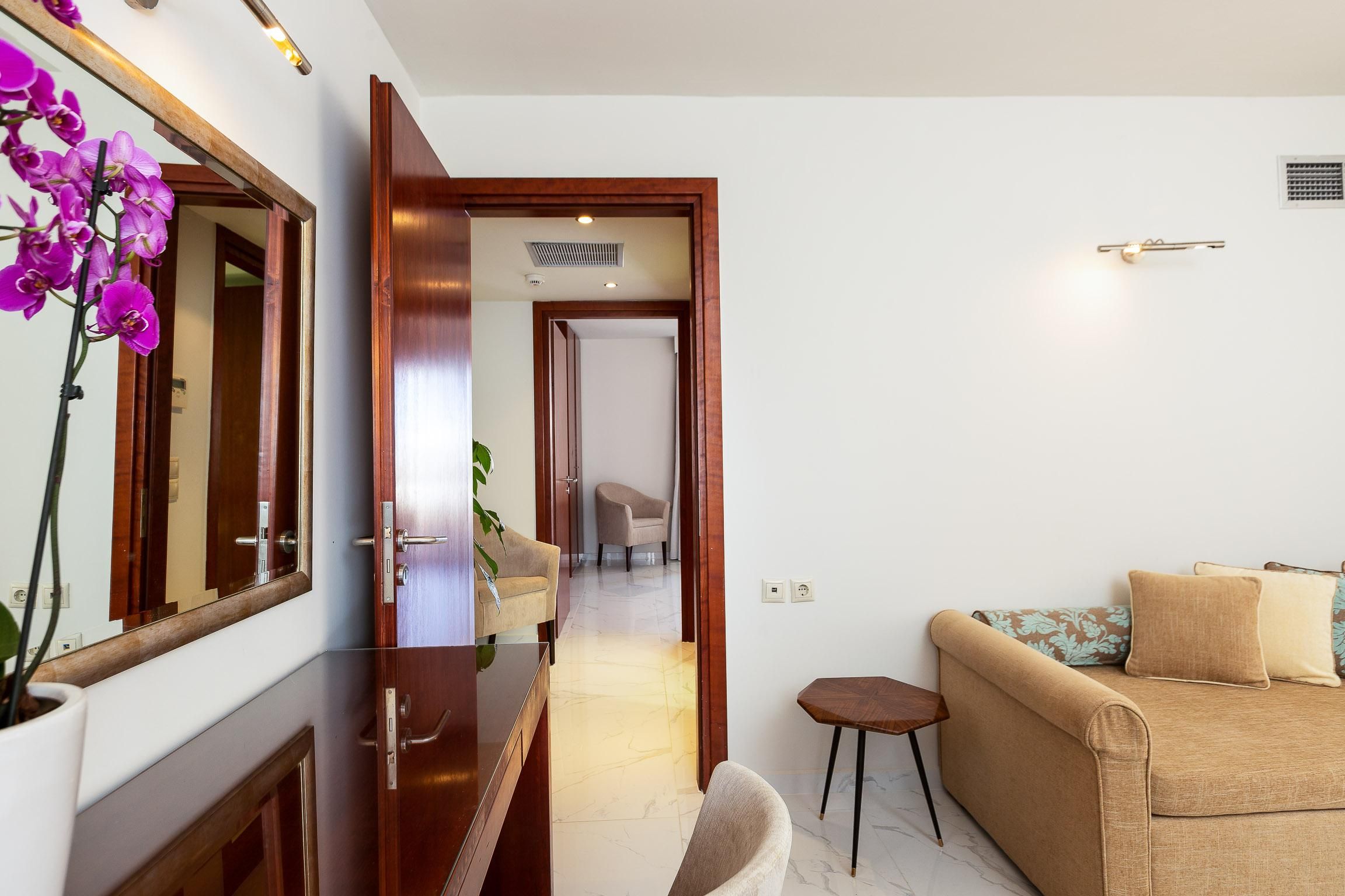 A modern living room with a sofa, a small side table, and a mirror with orchids.