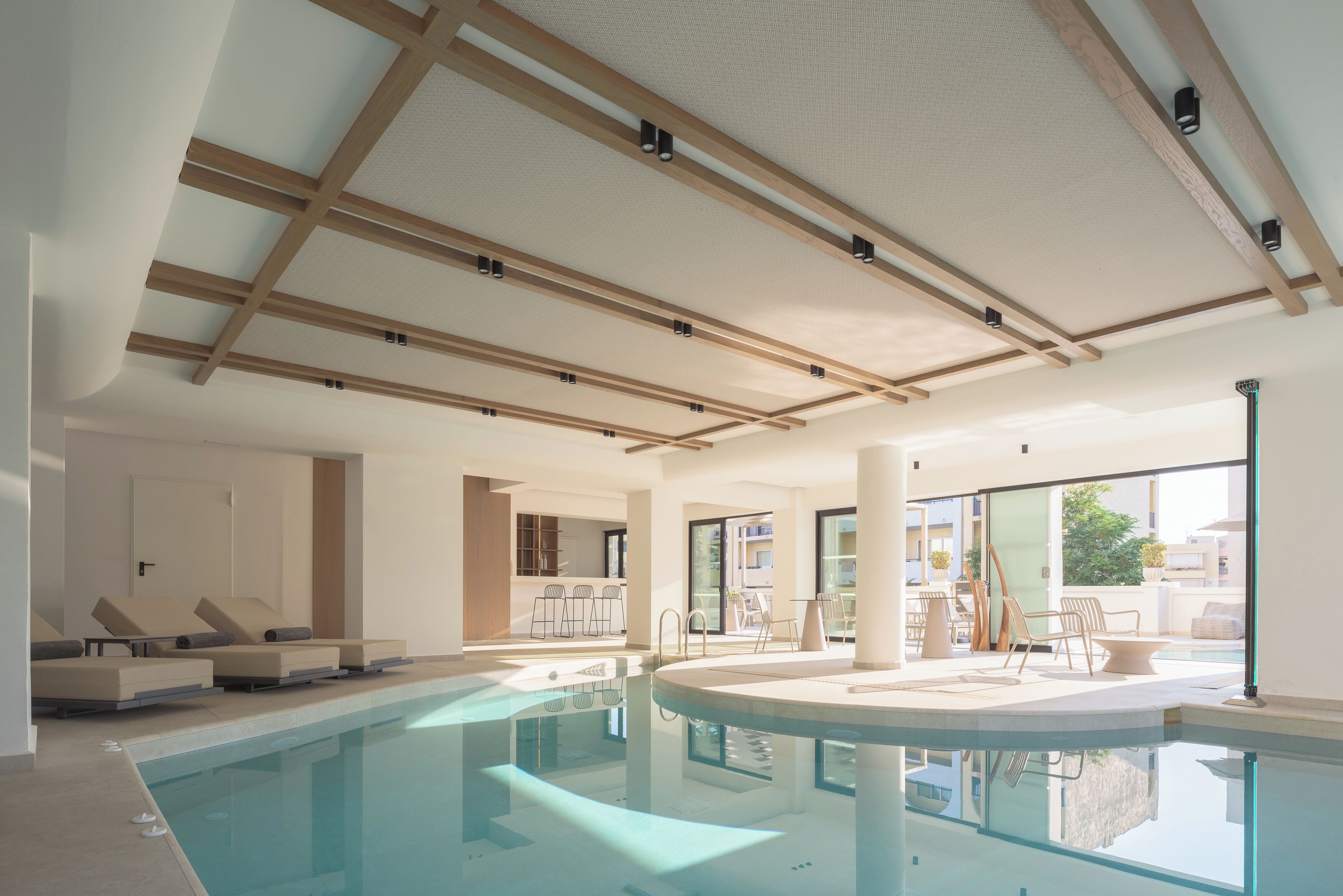 A modern indoor pool area with lounge chairs, a pool table, and a view of the outside.