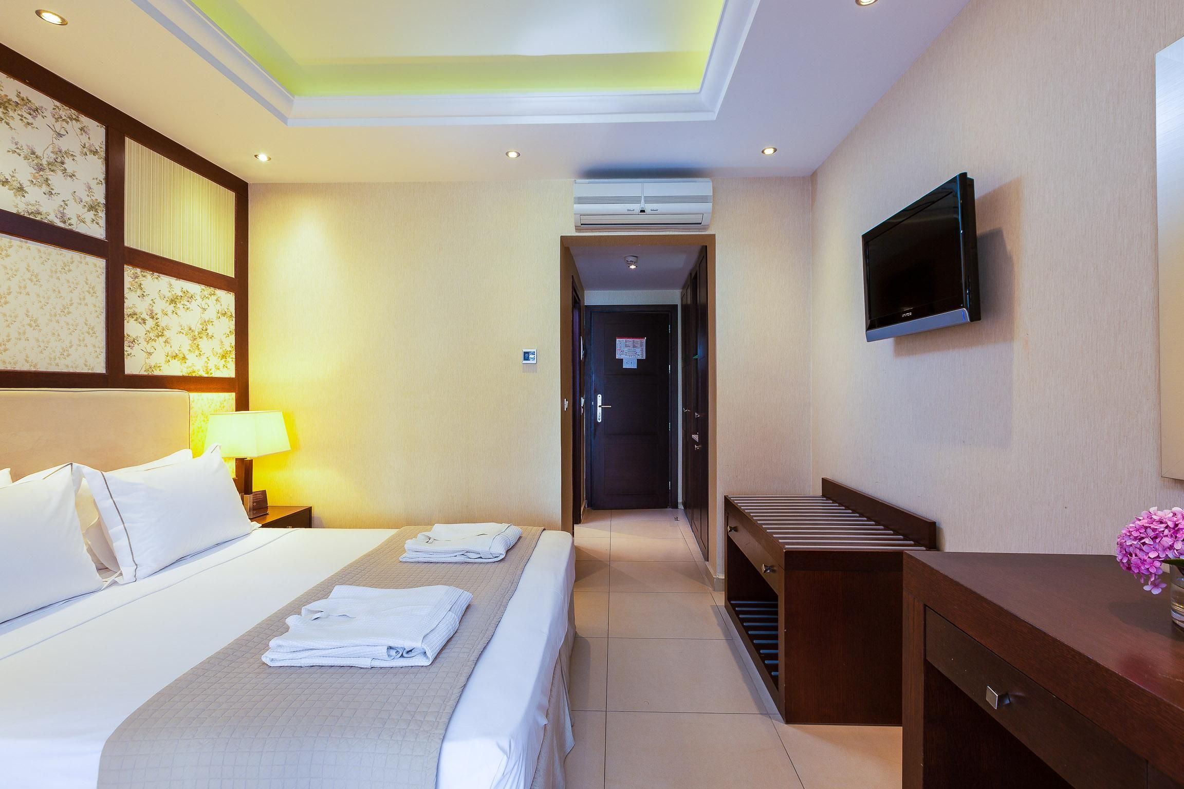 Habitación de hotel con cama, televisión, escritorio y baño visible a través de una puerta abierta.