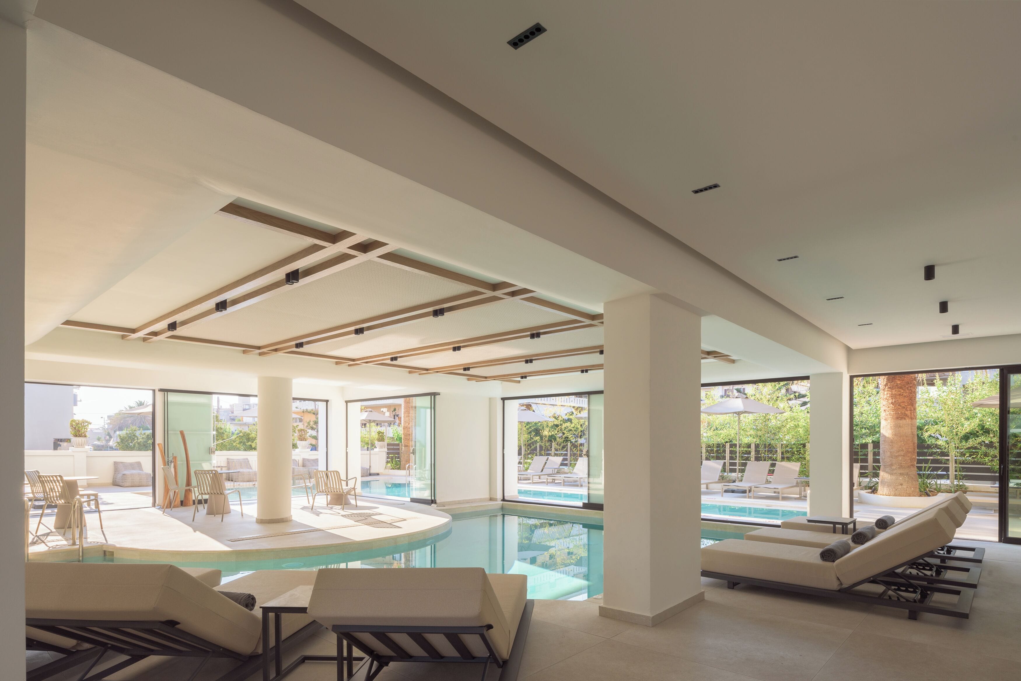 Un espace piscine intérieur moderne, doté de chaises longues, d’une table de billard et de grandes fenêtres offrant une vue sur l’extérieur.