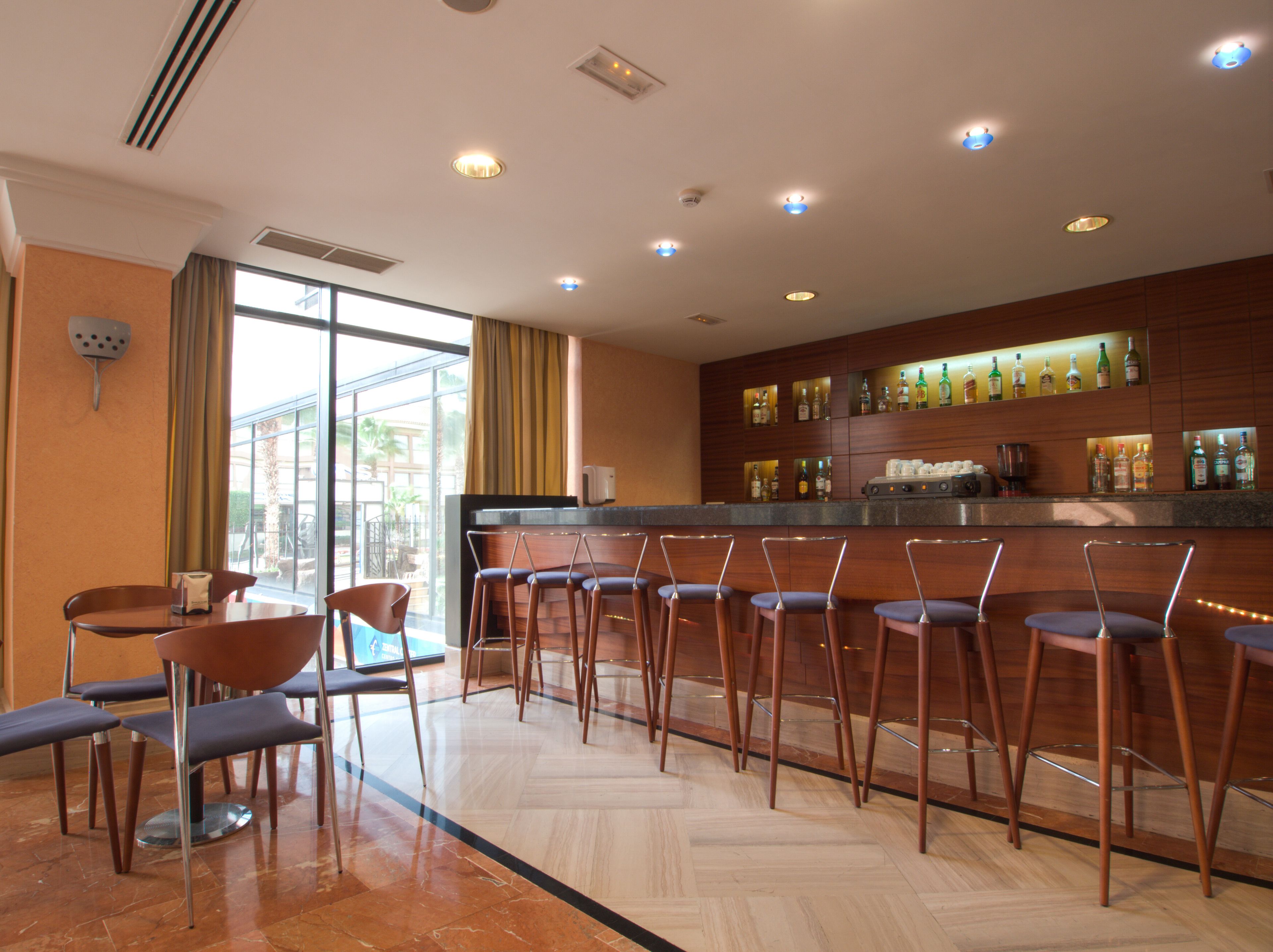 A bar area with multiple stools and a counter with bottles.