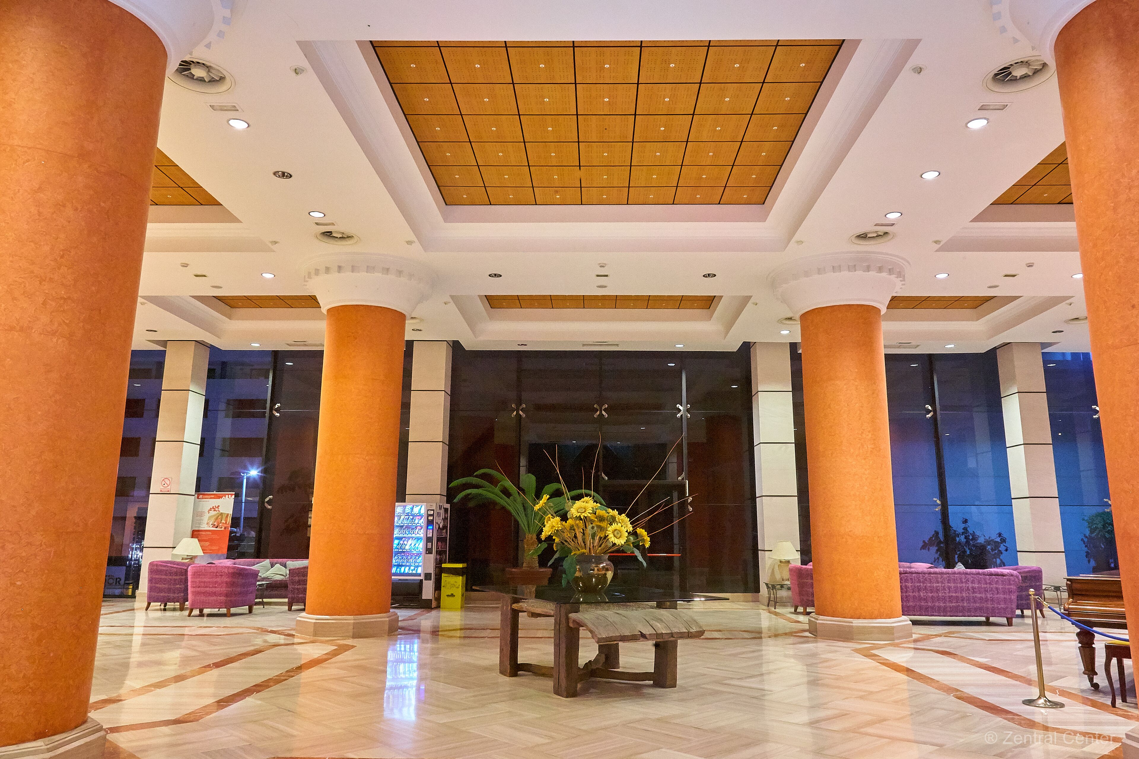 A lobby with large columns, a reception desk, and a seating area with purple chairs.