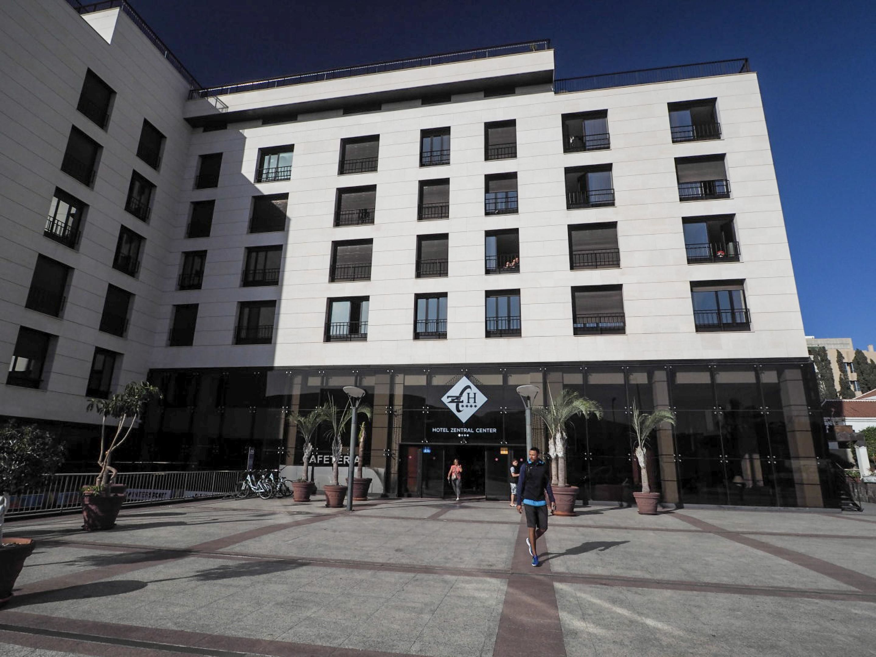 A modern hotel with a central entrance, multiple floors, and a clear sky.