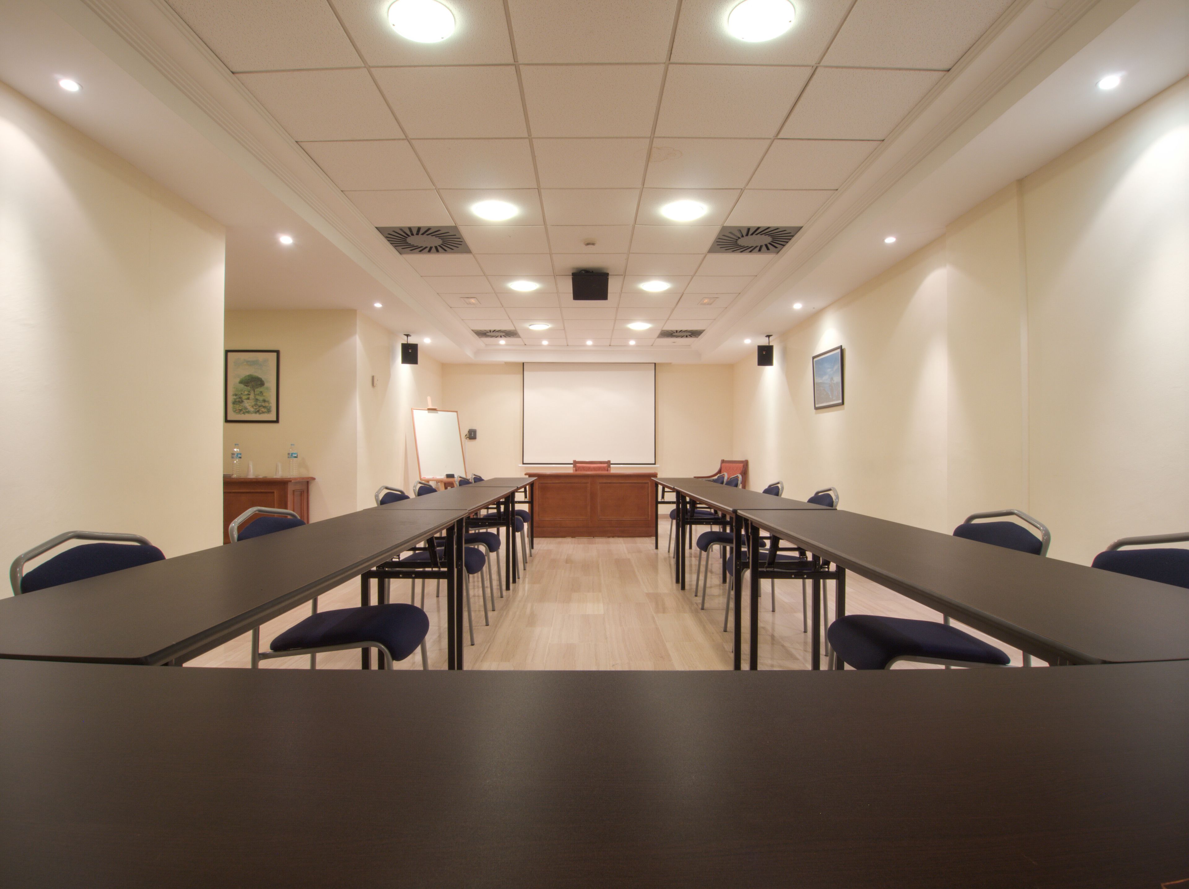A conference room with long tables and chairs, a whiteboard, and a projector screen.