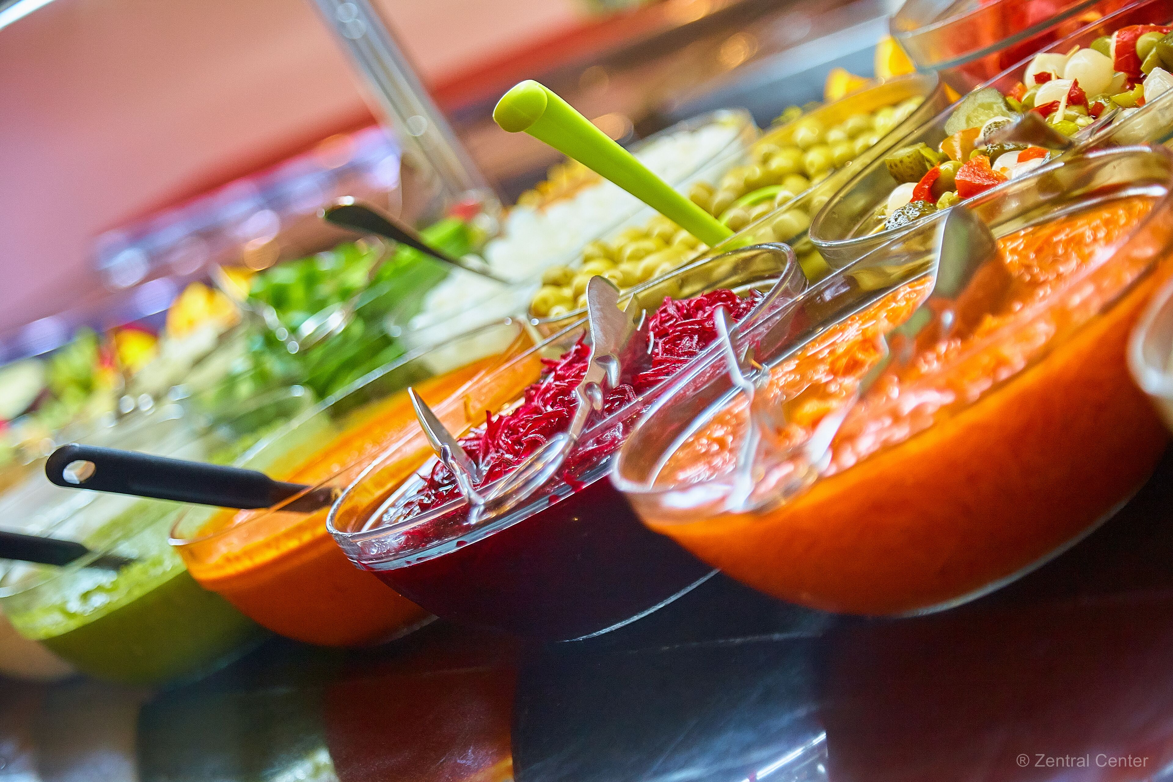 A buffet with various food items in clear containers, each with a serving utensil.