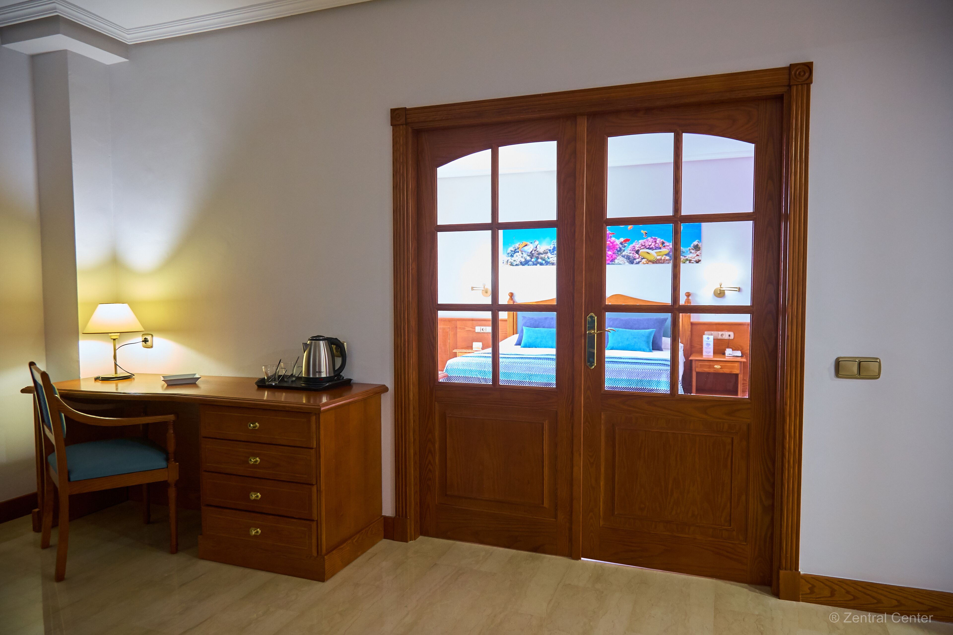 A room with a wooden desk, chair, and a large wooden door with glass panels.