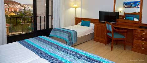 Een hotelkamer met een bed, een bureau, een stoel, een televisie en een groot raam met uitzicht op gebouwen.