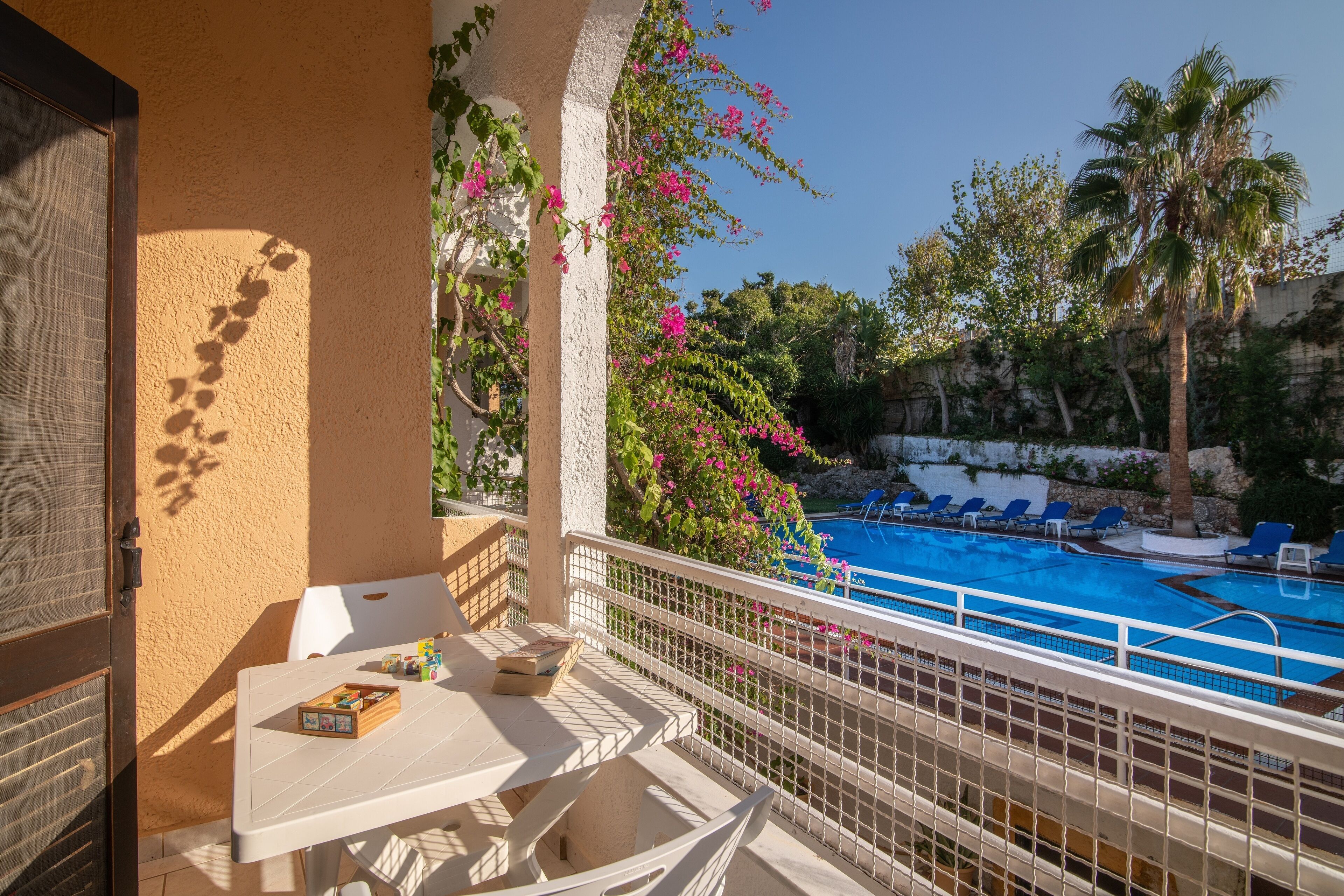 A balcony with a table and chairs, overlooking a swimming pool with lounge chairs.