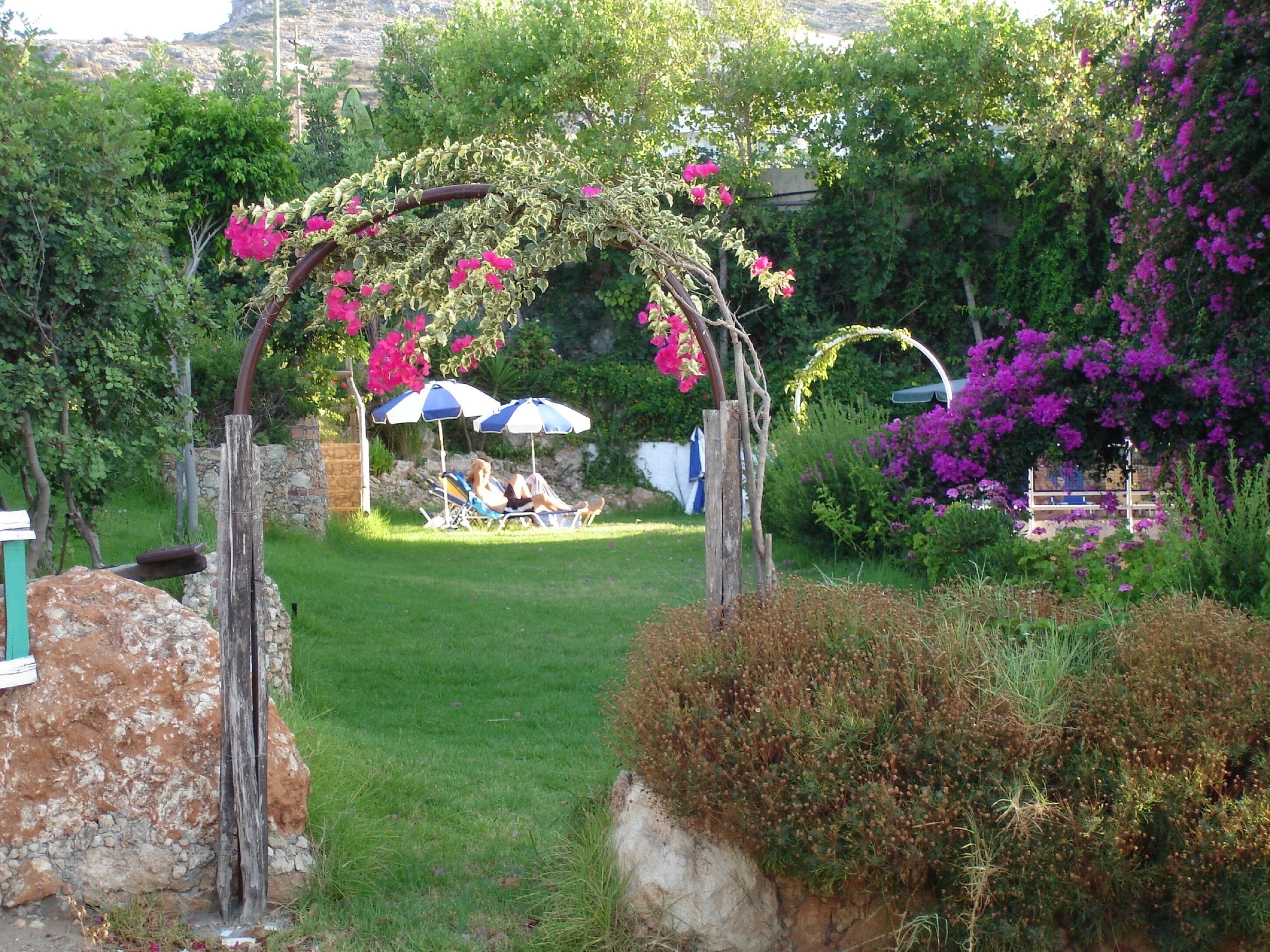 A garden with a pergola covered in flowers, a lawn, and a seating area with umbrellas.
