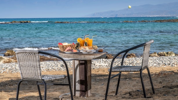 A table with food and drinks on a beach with a view of the sea and mountains.
