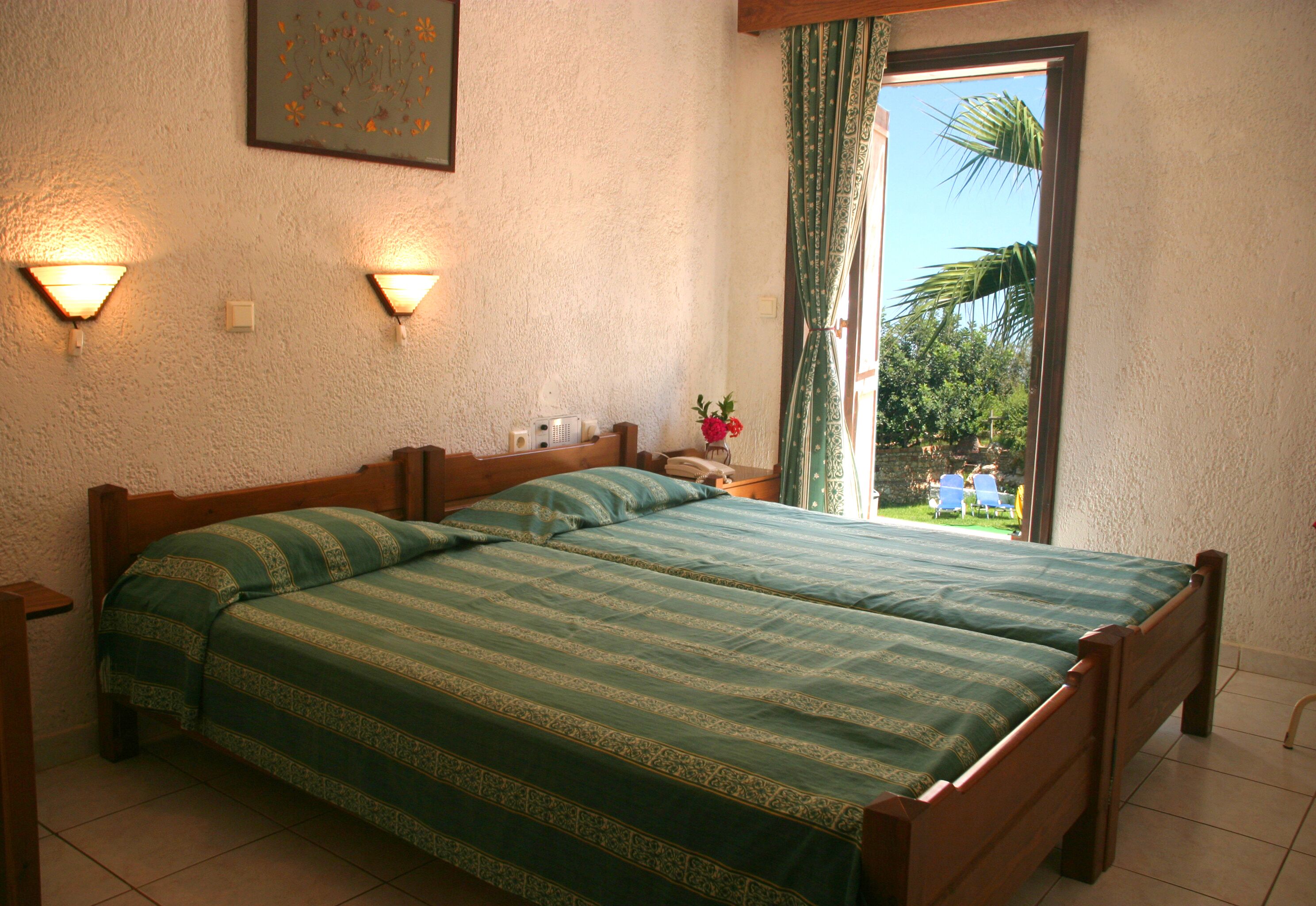 Un dormitorio con dos camas, una mesita de noche, una lámpara, una ventana con cortinas y vistas al exterior.