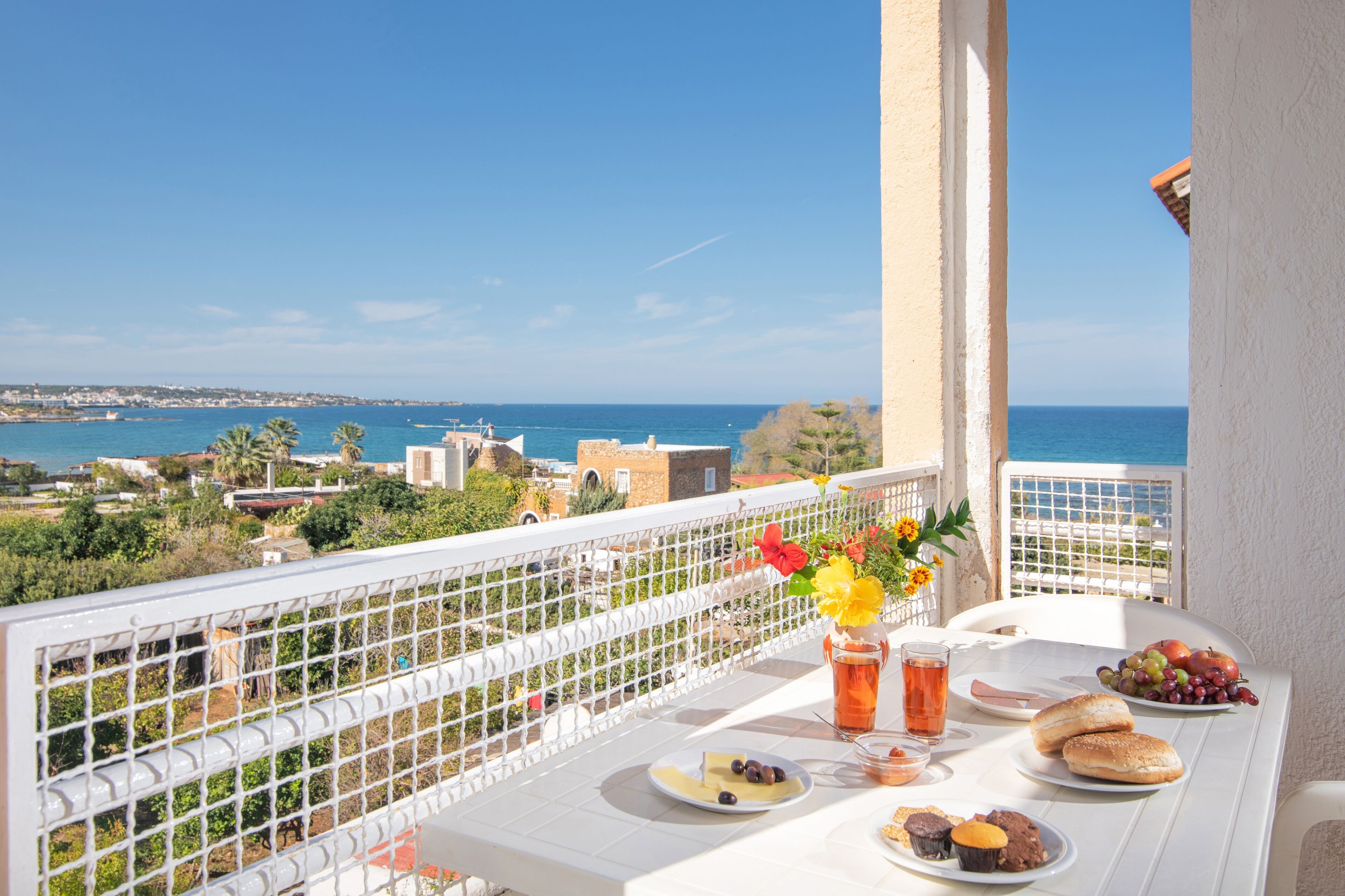 A balcony with a table set for breakfast, overlooking a coastal view.