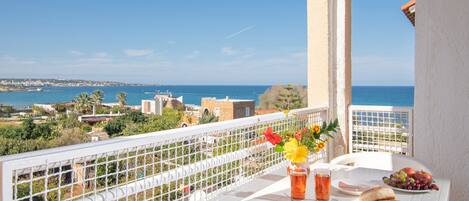 A balcony with a table set for breakfast, overlooking a coastal view.