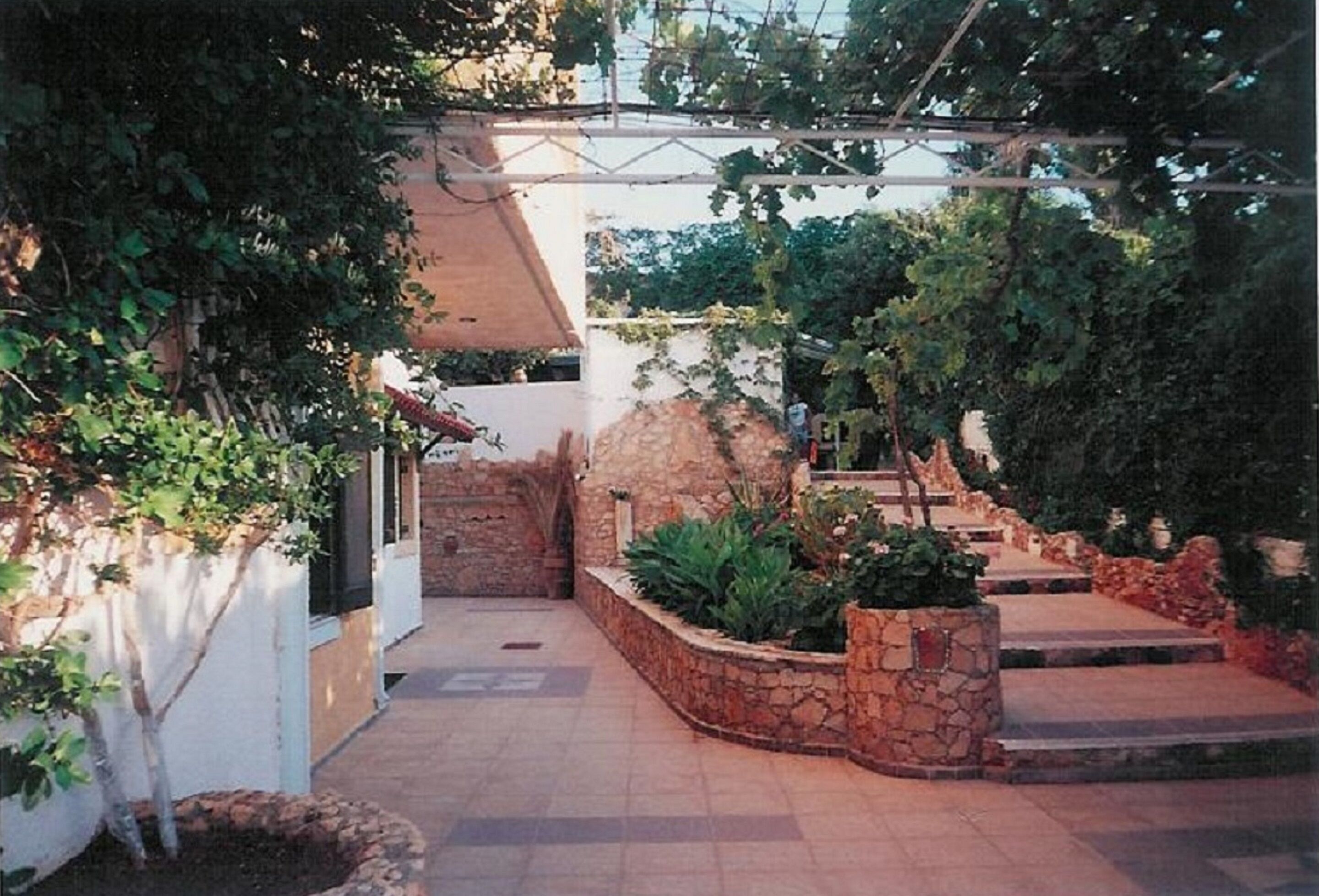 A courtyard with stone walls, a pergola, and a variety of plants.