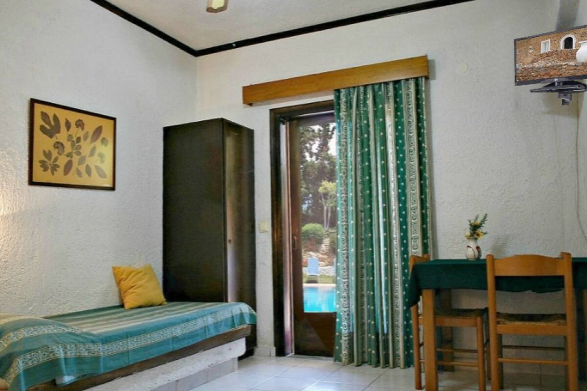 Una habitación pequeña con una cama, una mesa con una silla, un cuadro en la pared y una ventana con cortinas.