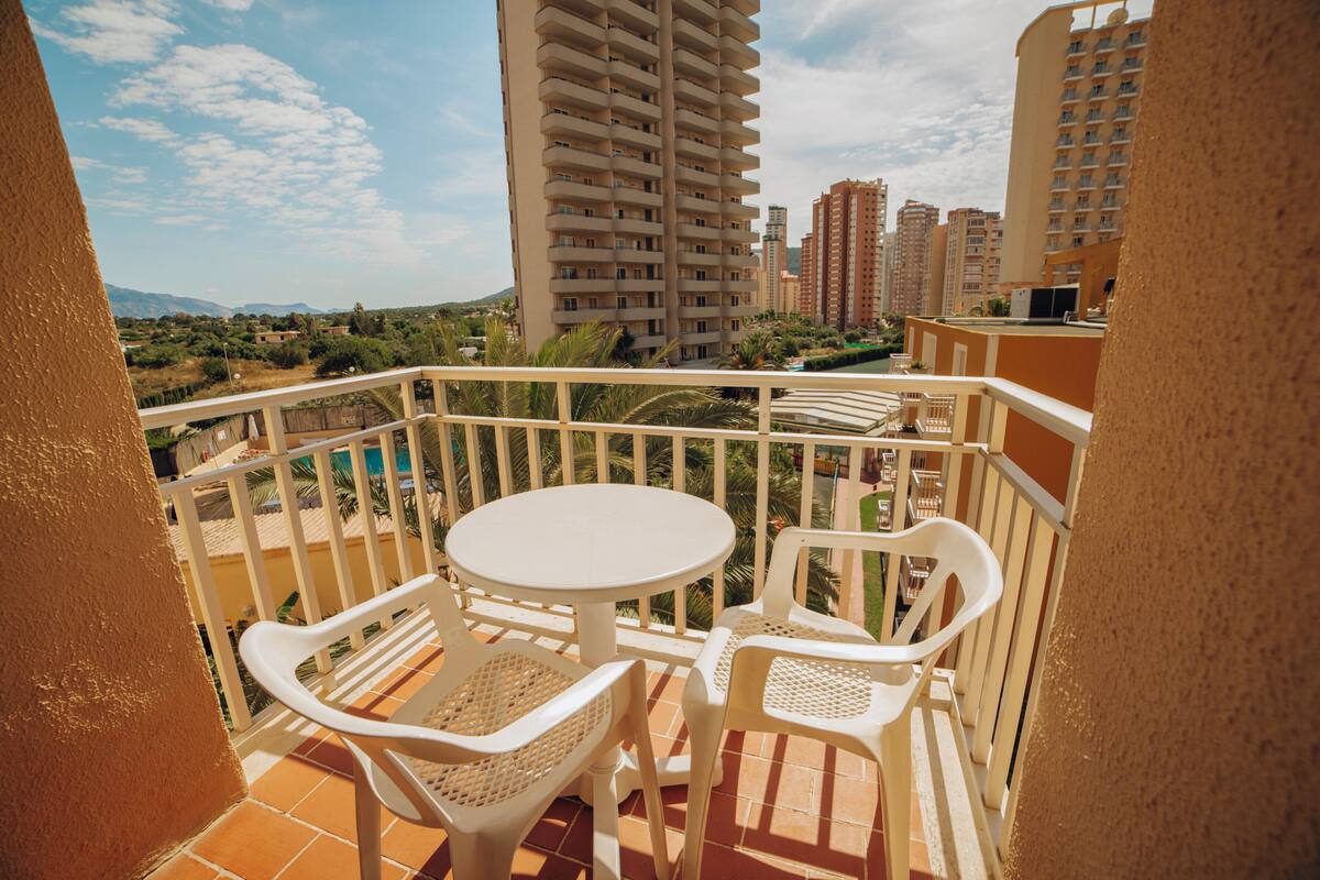 A balcony with a white table and chairs, overlooking a pool and surrounding buildings.