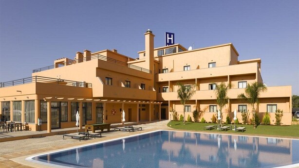 A hotel with a swimming pool, outdoor seating, and a 'H' sign on the roof. - Praia Sol (Vilamoura)