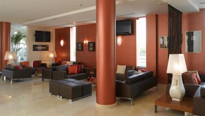 A modern hotel lobby with a large central column, multiple sofas, and a television mounted on the wall. - Praia Sol (Vilamoura)