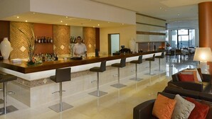 A modern bar area with a bartender, bar stools, and a seating area with sofas and a coffee table. - Praia Sol (Vilamoura)