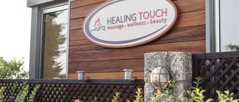 Letrero que dice 'Healing Touch', con un logotipo de una persona y una gota de agua, indicando servicios de masaje, bienestar y belleza.