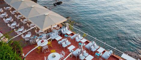 An outdoor terrace with tables and chairs, overlooking a body of water.
