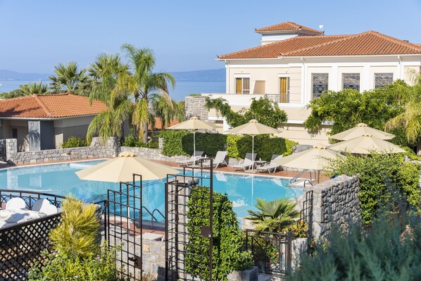 A pool area with lounge chairs and umbrellas, surrounded by greenery and a view of the sea. - Akti Taygetos Conference Resort (Kalamata)