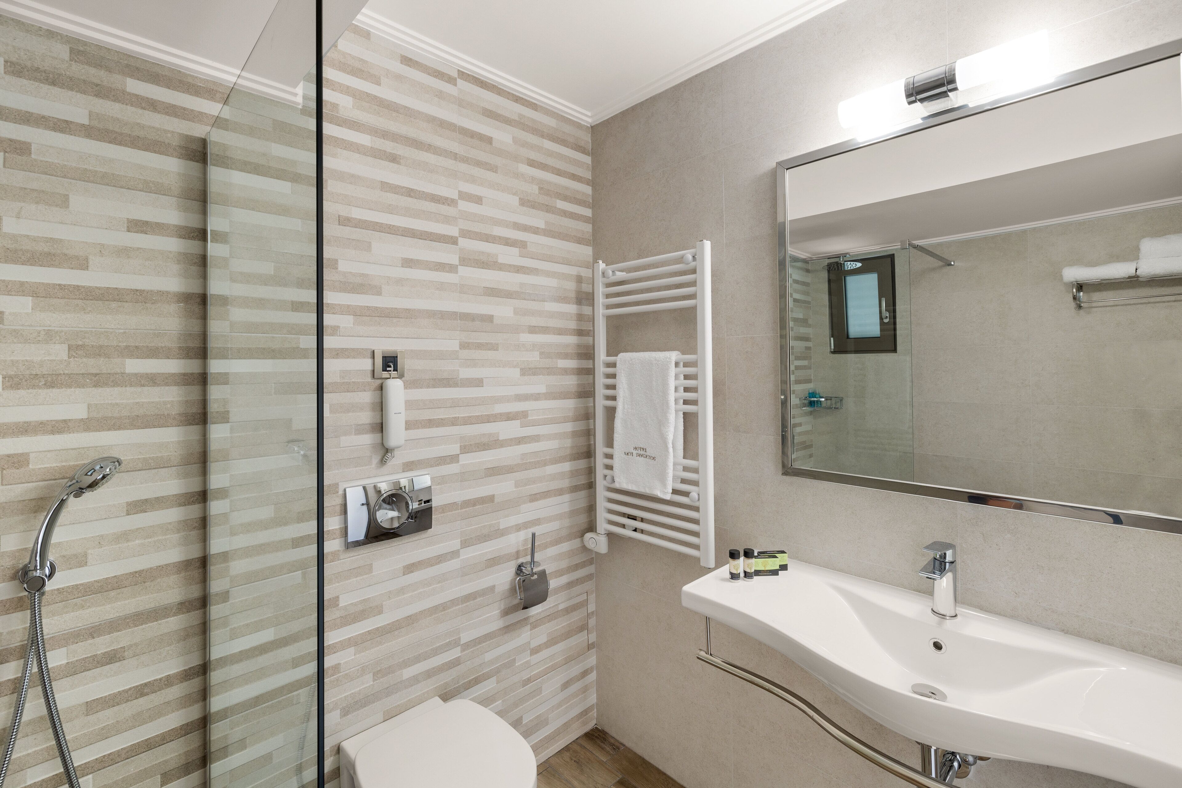 A modern bathroom with a glass shower enclosure, a white sink, and a towel rack.