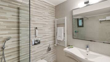 A modern bathroom with a glass shower enclosure, a white sink, and a towel rack.